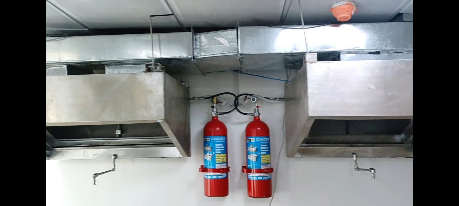 Two kitchen fire suppression cylinders installed between extraction hoods